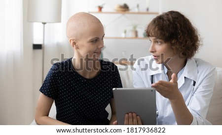 Doctor and young hairless sick female cancer patient look at tablet screen discuss treatment or cure together. Caring nurse talk with ill bald woman suffer from oncology, consider good results on pad. Royalty-Free Stock Photo #1817936822