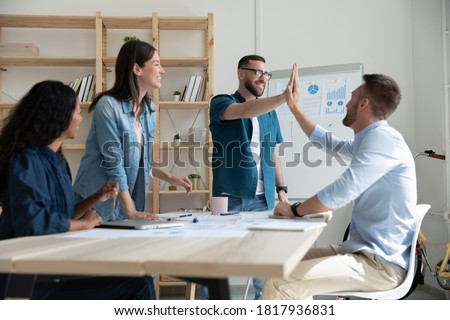 Happy colleagues giving high five at meeting, celebrating success, business achievement, diverse employees working with project stats, financial report together, engaged in team building activity Royalty-Free Stock Photo #1817936831
