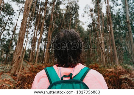 A super close up of the back of an old woman in front of a massive forest with a backpack and sport clothes