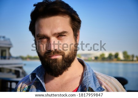 Portrait of bearded caucasian man with river and blue sky at background.