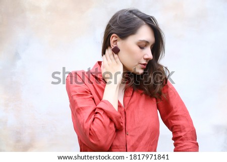 young woman brunette in a red shirt on a light background looks sideways and holds her hand to her hair.