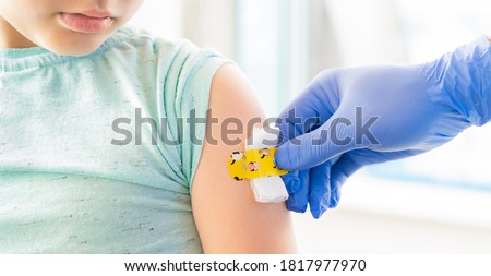 Vaccination of little girl in doctor's office.Kids funny adhesive plaster,gauze napkin.Hand in glove.Vaccine for covid-19 coronavirus,flu,infectious diseases.Injection.Clinical trials for human,child.