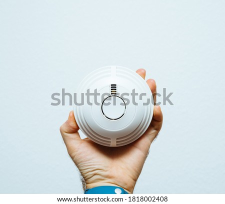 Male hand holding smoke fire alarm in hand against white background - front view of the device