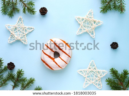 Christmas and new year's composition. Donut in white glaze, decorative wicker stars on a blue background with spruce branches and cones in the form of a frame. The view from the top.