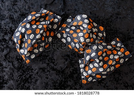 Three orange and cream colored pumpkin patterned fabric face masks on a black background
