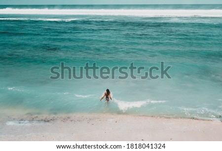 
Young woman in a bikini at the white sand near the waves of blue sea. Bali, Indonesia. Aerial Shooting. Stunning tropical beach view. Top view aerial photo  flying drone an amazingly beautiful beach