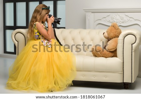 A snapshot of an unidentified young girl using a camera to take a picture of her Teddy.