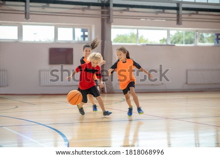 After the ball. Kids in bright sportswear playing basketball together and running