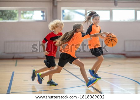 Game. Kids in bright sportswear playing basketball together and feeling competitive