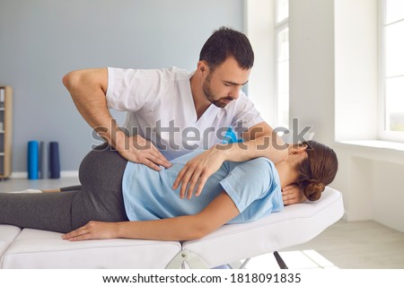 Young man doctor chiropractor or osteopath fixing lying womans back with hands movements during visit in manual therapy clinic. Professional chiropractor during work Royalty-Free Stock Photo #1818091835