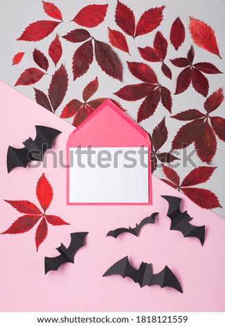 Holiday decorations, bats, empty blank card in paper envelope on pink background. Halloween party greeting card mockup with copy space. Happy Halloween concept. Flat lay, top view, overhead.