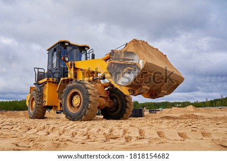    powerful yellow bulldozer crumbles sand at construction site                                Royalty-Free Stock Photo #1818154682