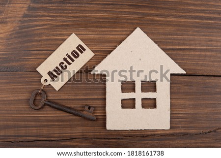 Auction - text on the key label. House model and old key on wooden background - real estate buy or rent concept