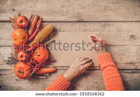 Autumn background, fallen leaves, fruits, vegetables on rustic wooden table. Woman hands with aged vintage paper and pencil, copy space. Thanksgiving food, healthy and fresh, top view, flat lay.