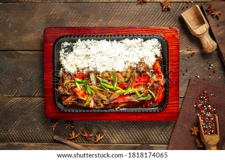 Top view on roasted beef with vegetables and rice in cast iron pan