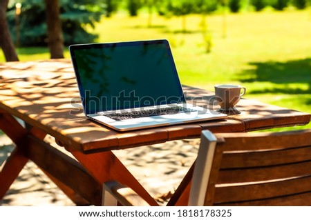 View on a laptop pc and a coffee mug on a table in the garden in a home office or home school enviroment on a sunny day.