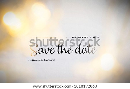 Save the date - Black text between yellow bokeh Christmas lights on a white textured paper background