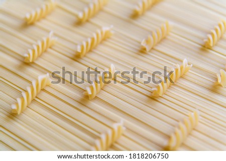Raw uncooked fusilli pasta (also known as rotini) lies on raw spaghetti pasta. Abstract food background. Selective focus. Copy space for your text. Italian cuisine theme.