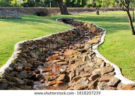 Small creek, with water flowing with a purpose built stone structure to control flooding and run-off of water.
Parks and gardens environment control. Royalty-Free Stock Photo #1818207239