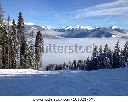 Panoramic view of snow-covered ski black slope in Dolomites at Plan de Corones (Kronplatz) ski resort South Tyrol, Italy. Winter landscape on a sunny day with low clouds in the valley of Bruneck.