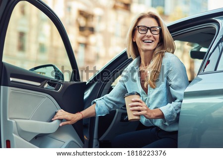 Happy attractive woman or business lady wearing eyeglasses holding cup of coffee and getting out of her modern car Royalty-Free Stock Photo #1818223376