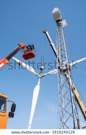 Construction of a wind power plant. Installers use a truck crane and aerial platform to raise the wind turbine rotor. Photo taken on a sunny summer day in Russia Royalty-Free Stock Photo #1818240128