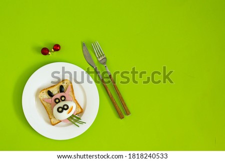 New Year's funny breakfast toast for kids. Creative children's sandwich in the shape of a bull made from toast, sausages, eggs on a green background. Bull cow Symbol of the year 2021, copy space