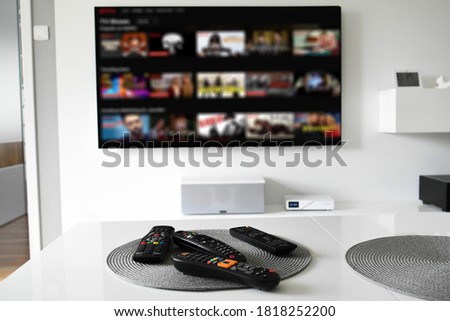 TV remote controllers on table with blurred streaming service on television in the background, a selective focus picture. Royalty-Free Stock Photo #1818252200