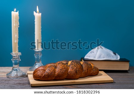Shabbat Shalom. Challah bread, shabbat wine and candles on wooden table. Lighting a candle