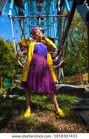 Portrait of a stylish model in a yellow coat posing against the backdrop of amusement park 