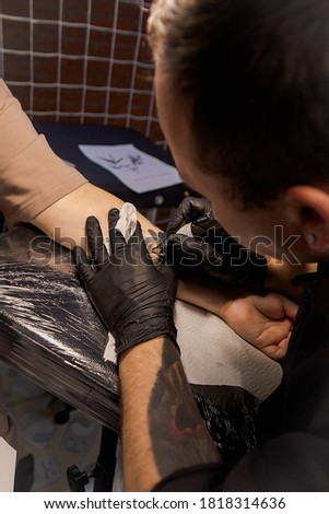 Professional tattoo artist makes a tattoo on a woman's hand