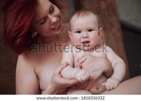 Mom holds the baby in her arms and looks at him tenderly, the baby smiles at the camera