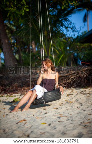 Beautiful woman sitting on the swing on paradise beach