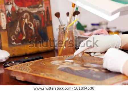 Art restorer working on the ancient icon with spatula at workshop