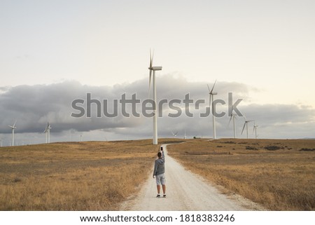 Wind farm with windmills. A person is taking a picture with his mobile phone on a road to the windmills.