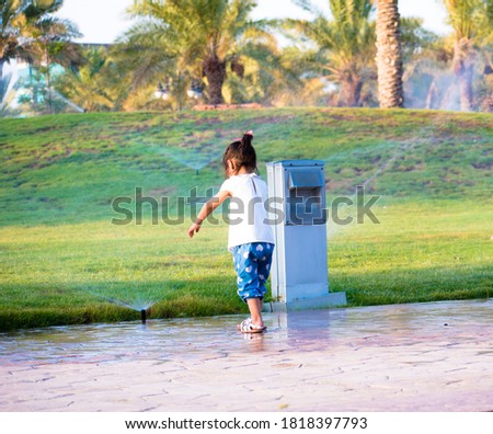 Picture of a curious little girl reaching her arm to a water sprinkler.
