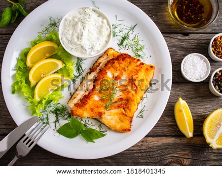 Fish dish - fried cod fillet with cream sauce and lemon served on wooden table 