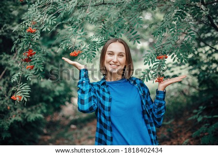 Autumn fall woman portrait. Beautiful happy smiling middle age woman standing in park with red rowan berries on her ear. Silly funny moment. Woman in park outdoor. 