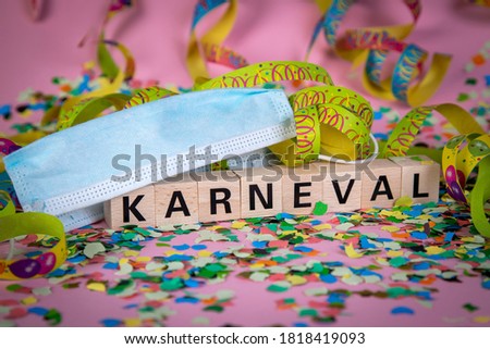 German word KARNeVAL on wooden blocks under a face mask with confetti and streamers, pink background