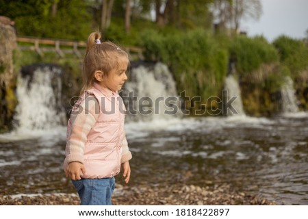 Little girl playing near the water, 
throw stones into the river.