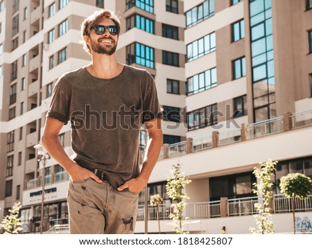 Portrait of handsome smiling stylish hipster lambersexual model.Man dressed in green shirt. Fashion male posing in the street at skyscraper background in sunglasses. Outdoors at sunset 