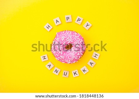 pink delicious donuts on yellow background and inscription from wooden blocks happy hanukkah