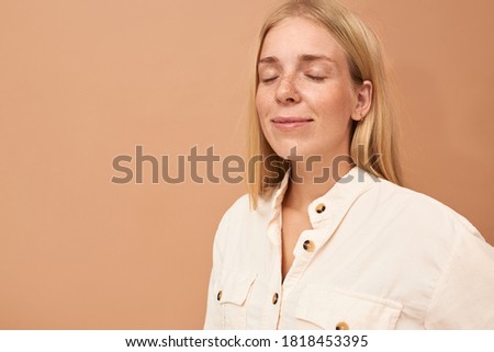 Beautiful young female with freckles and straight hair keeping her eyes closed and smiling, dreaming about vacations, thinking of something pleasant, having peaceful look. People and lifestyle concept