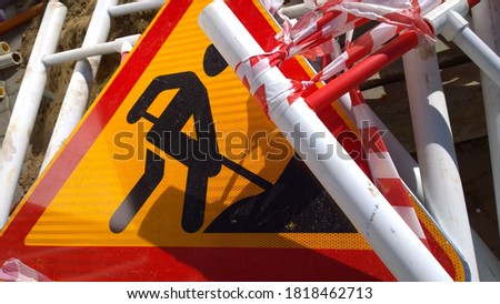 Road works sign denoting construction work and metal fencing on the ground. Close up. Red and yellow сolour. Restoration and reconstruction concept. Traffic barrier. Providing security control. 
