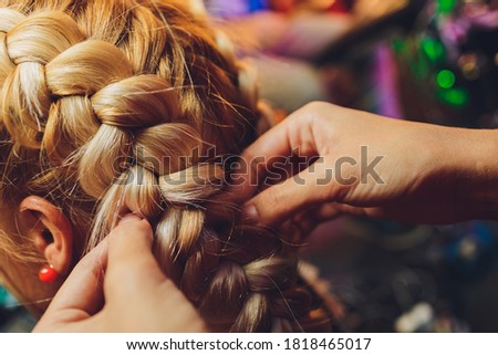 Process of braiding the master weaves braids on her head blond little girl in beauty salon close up. Professional hair care and creating hairstyles.