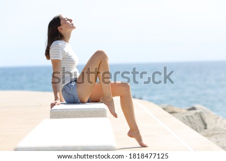 Profile of a happy woman with long waxed legs breathing fresh air sitting on a bench on the beach Royalty-Free Stock Photo #1818477125