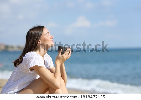 Side view portrait of a relaxed girl smelling coffee on the beach on summer vacation Royalty-Free Stock Photo #1818477155