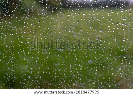 Rain drops on car window glass surface with green rice field blurred background, natural pattern of raindrops.