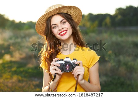 smiling woman in hat with camera in hands yellow t-shirt nature