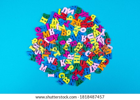Chaotic pattern of English letters on a blue background. The Latin letters are arranged in a circle in the middle of the blue sheet. Learning to read and write. Reading of books.
